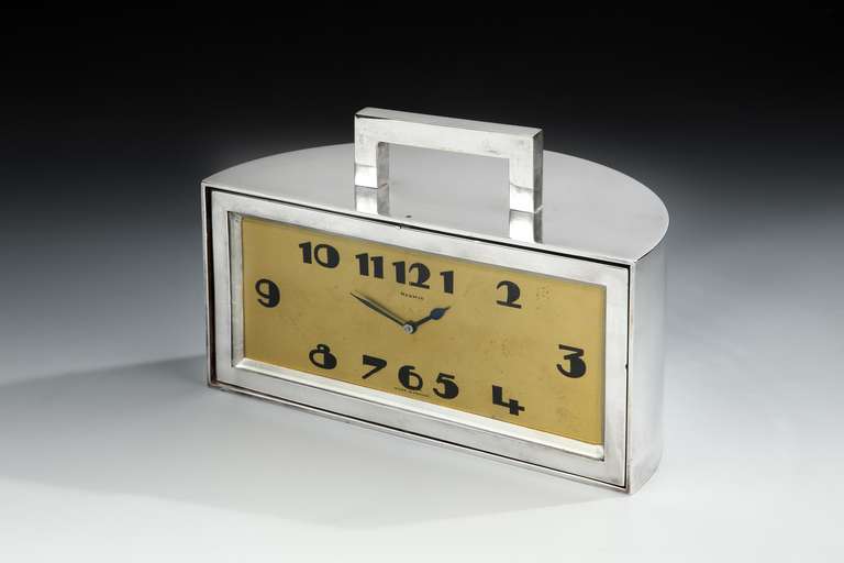 A fabulous and unusual Art Deco demilune mantel or desk clock, the heavy nickeled bronze mechanical movement clock with angular top handle, with wide, stylized Art Deco clock face and numerals, rotating to reveal a hidden wood lined trinket or