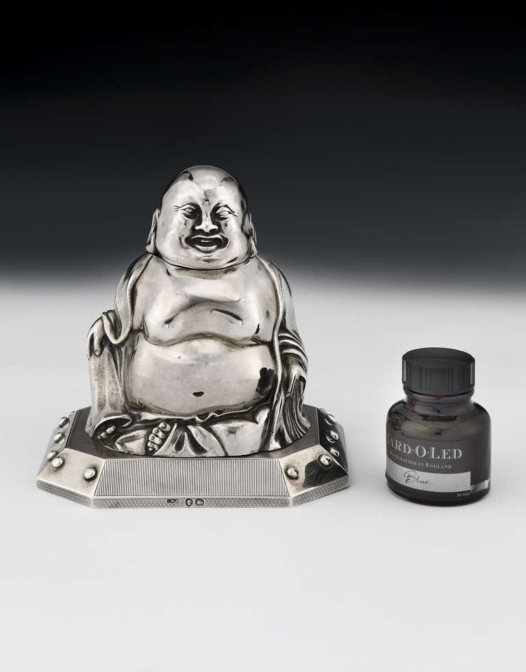 An early and most likely unique, special-commission Sterling silver match striker in the form of a smiling, seated Buddha, the head hinged to reveal a void in which to put matches, the body resting on an hexagonal engine-turned plinth. Bearing marks