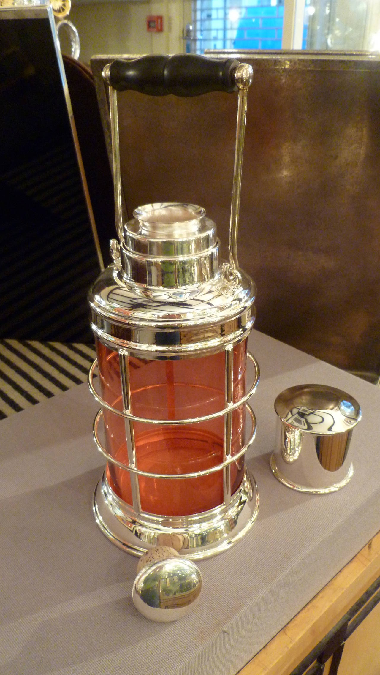 A rare, novelty silver-plated cocktail shaker in the form of a traditional ship’s lantern, with a ruby-red glass liner, with a silver plated, cork-lined cap and integral strainer, and loop handle with wooden grip. Stamped ASPREY & Co, LONDON to the
