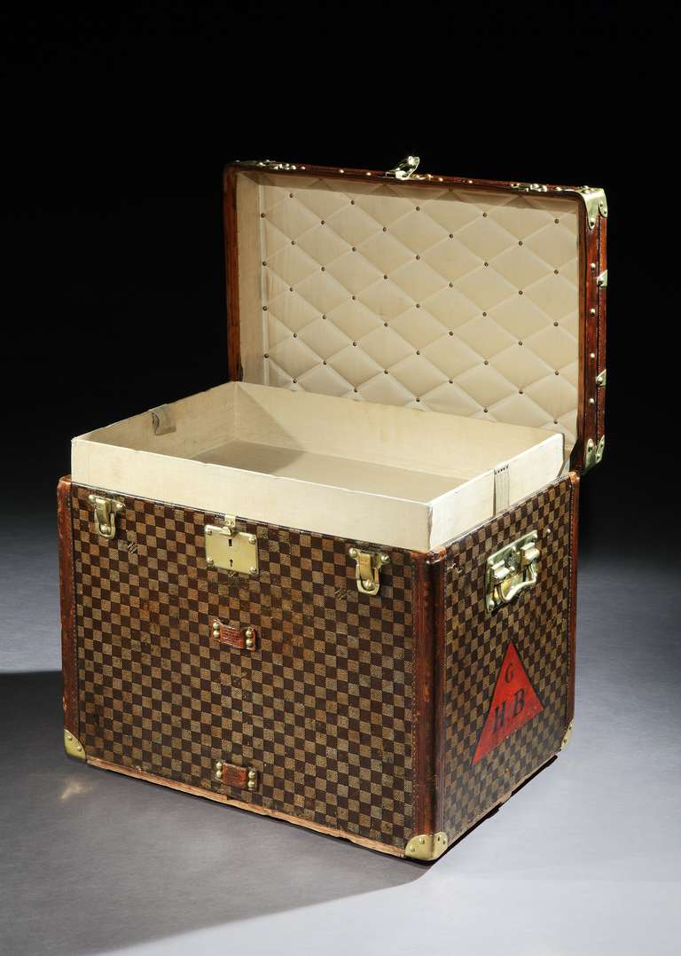 A rare 'Cube' trunk in early ‘Damier’ patterned canvas, with leather trim and all-brass handles and corners, with the original owner’s initials of ‘G.H.B’. in black, set within a red triangle to one end. French, circa 1890.
.