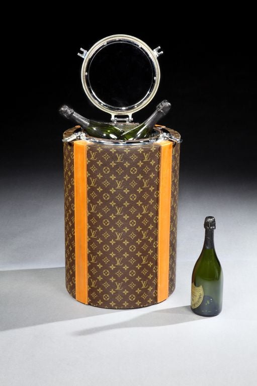 A very stylish and unusual ‘Porthole’ wine or Champagne cooler by Louis Vuitton. The barrel covered in Vuitton ‘Monogramme’ patterned canvas, with tan leather strap details, the chrome plated ‘porthole’ with a glass central window, so you can see