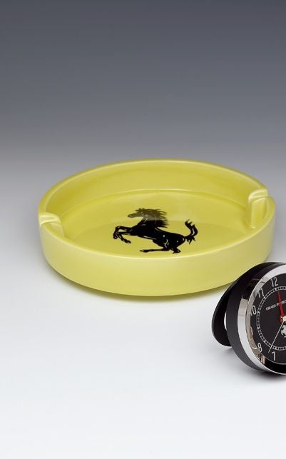 A stylish, large-scale ceramic cigar ashtray, glazed in Ferrari 'Giallo Fly' (Fly Yellow), with the Ferrari 'Cavallino Rampante' logo in black glaze to the base. 

Of recent manufacture (2000) and now discontinued. 

Complete with original