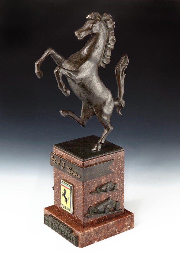 A highly important cast bronze Ferrari ‘Cavallino Rampante’ (‘Prancing Horse’) trophy,  set on a square marbre rouge plinth, with stylised bronze racing cars applied to three sides of the plinth, the front bearing enamelled Ferrari badge and legend