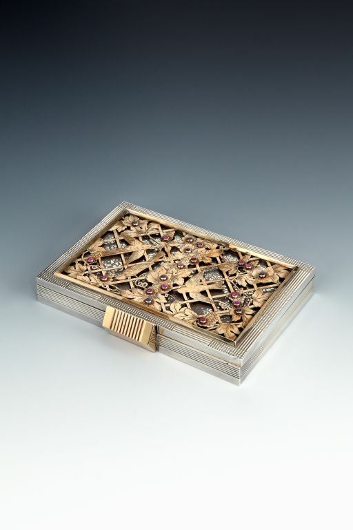 A French silver and silver-gilt and gem-set vanity compendium of rectangular form with reeded and chequered decoration, the cover with a central pierced gilt panel depicting birds amongst gem set fruiting vines on an open-work trellis, the interior