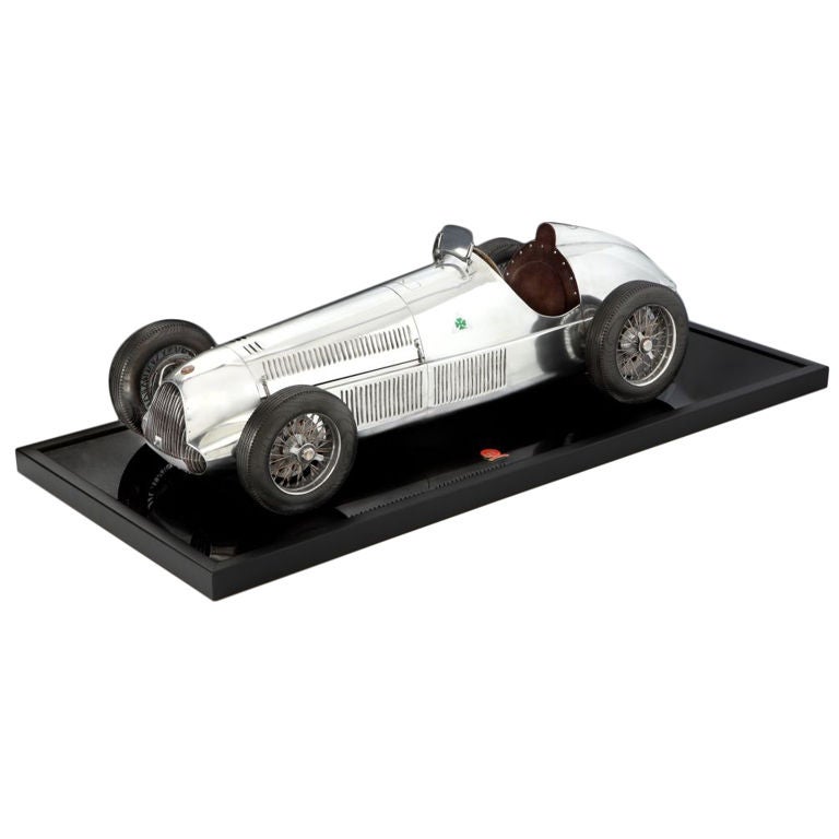 A large scale model of an Alfa Romeo 158/159 ‘Alfetta’ detailed in metal, and wood, with exhaust detailing, bonnet with sprung ‘stays’, the body in aluminium with brass accents, wooden ‘tyres’ with aluminium spinners, Alfa Romeo mascot badge,and