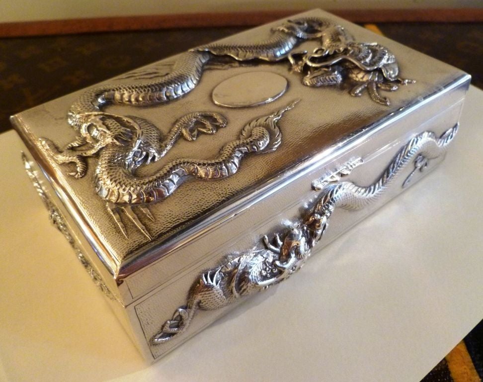 A very heavy gauge but intricately figured silver Chinese cigar or cigarette box, the main body in a hammered finish, overlaid with an ornate repoussé dragon motif to the top, with another two dragons woven on the sides, front and back, with a