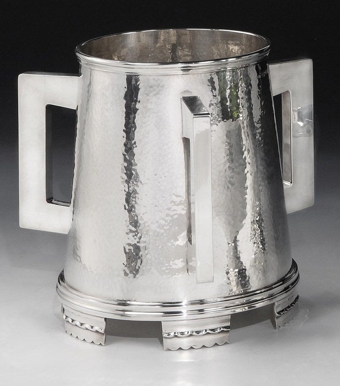 A very stylish and very large, three handled, Sterling silver trophy cup with geometric conical body with hammered finish, with three angular handles, and three feet with scalloped detailing. Bearing hallmarks 'KB' and London hallmarks for 1914. The