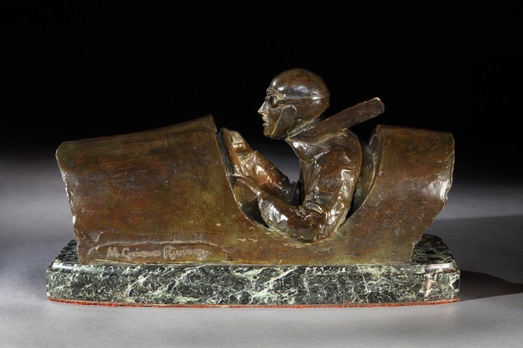 An important, dark patinated, hollow cast bronze Art Deco sculpture depicting a racing driver at the wheel, mounted on a shaped veined marble plinth, with crisp, impressed signature M. GUIRAUD RIVIÈRE in the bronze, and bearing foundry stamp to the
