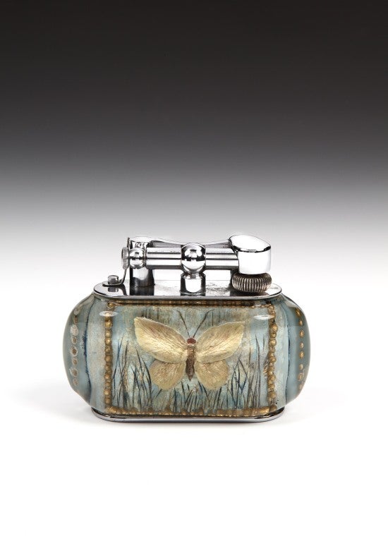 An extraordinarily rare silver-plated 'Aquarium' table lighter, very likely a unique experimental piece,of eliptical form, the perspex body enclosing hand-painted scenes to the front and reverse of a butterfly in flight against a pastel sky-blue