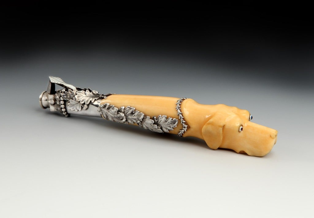 An unusually large late-1800’s Viennese silver mounted ivory cigar cutter in the form of a hound, the dogs headset with glass eyes, with a laurel leaf collar, and overlapping silver foliate mount, and the cutter section with beaded border with
