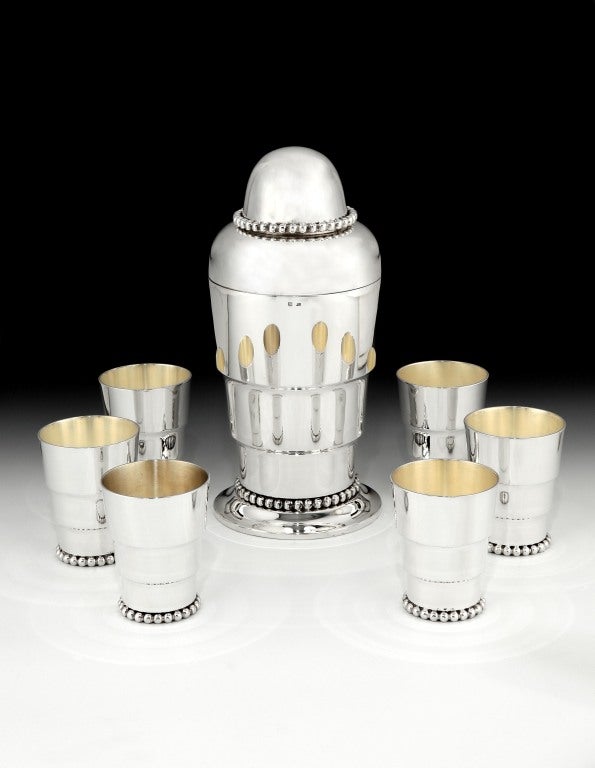 A classic silver plated Art Deco cocktail set, with stepped form and beaded detailing to the shaker and six cups, the shaker's cap with a bayonet fitting, to ensure a perfect seal when shaking.