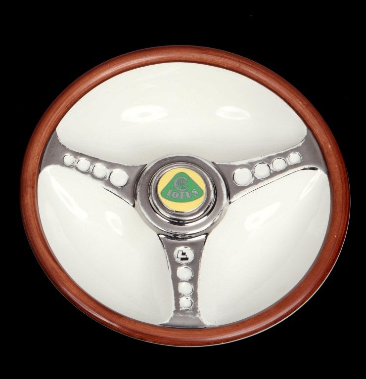 A promotional ceramic ashtray for the British car maker Lotus, in the form of a steering wheel, bearing a facsimile logo for the company in gilt and green glaze to the centre of the wheel. English, circa 1950s. Bears Beswick marks to the base, along