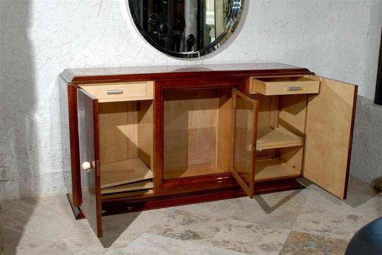 A French Art Deco period walnut sideboard with onyx top and three doors from the 1930s. This French sideboard features a raised rectangular inset wavy red onyx top over two light walnut doors flanking a central glass door. Each lateral door is