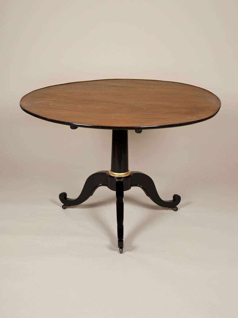 A 19th century faded mahogany circular tilt top table with an ebonised and parcel gilt tripod base.