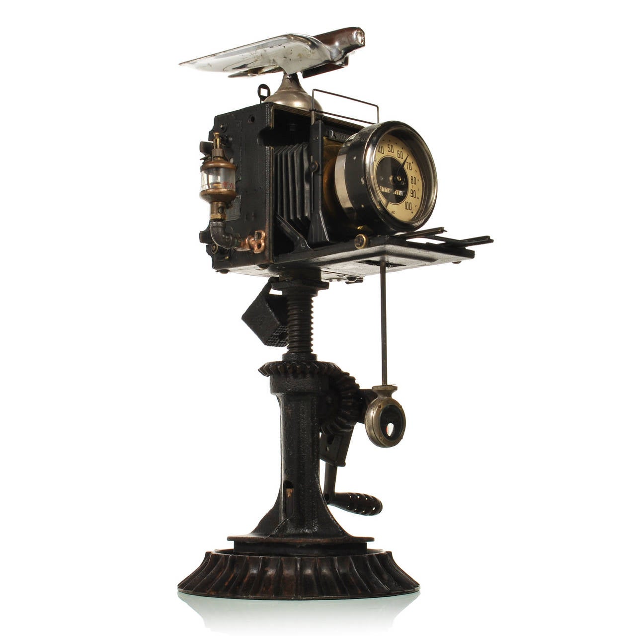 This unique automotive influenced sculpture is made of various antique car parts. The center piece is an antique 4 x 5 Speed Graphic camera by Graflex. The large format camera with its accordion bellows houses a working clock with a pendulum made