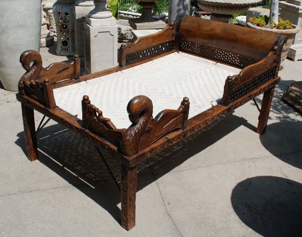 Indian carved bed with a woven sleeping platform and iron supports.