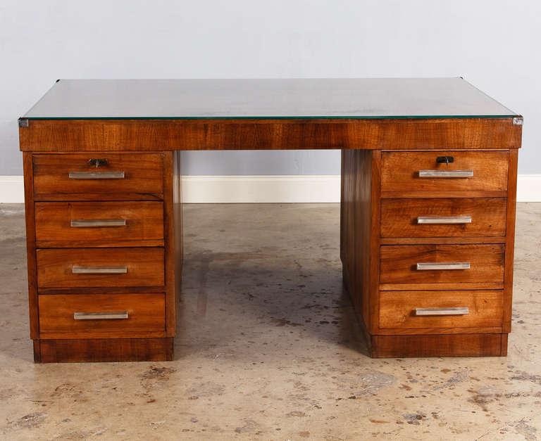 A great French Art Deco Desk in walnut wood veneer from the Beaujolais region. The knee hole is flanked by two sets of 4 drawers with chrome metal handles. The glass top is beveled. Each side has a pull out shelf made of stained pine wood (each