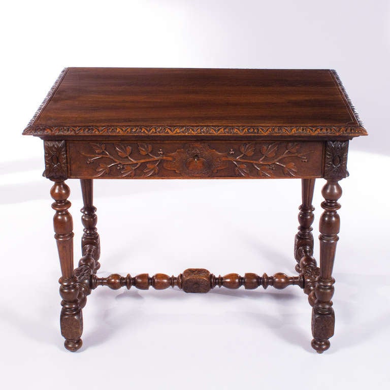 A small Desk made of carved walnut with a gorgeous patina from the late 1800's. The Writing Table has a H-shaped stretcher, turned baluster legs and gadrooning carvings with floral motifs on the apron. The single drawer has its key.