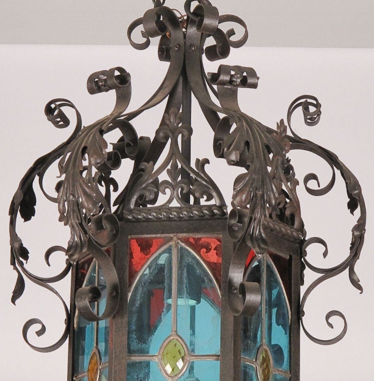 A forged iron Neo-Gothic Lantern with scrolls and acanthus leaves motifs. The six stained glass panels are framed with lead. One panel can be open for access to light bulb. Height varies with adjustable chain.