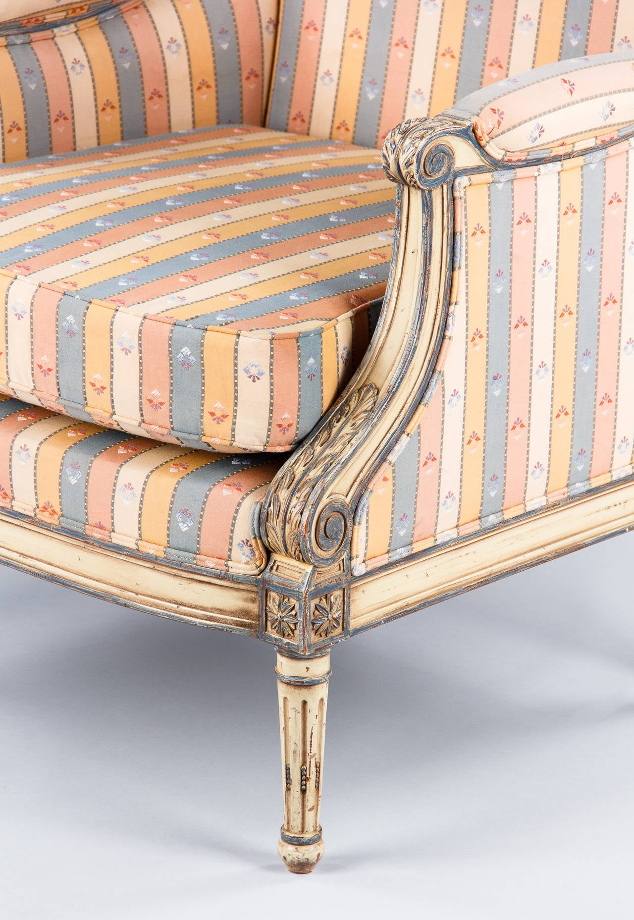Created back in the 18th century, the marquise is similar to the bergère but lower and wider. This mid-1900s marquise in the Louis XVI style is painted in off-white and light blue tones. The legs are fluted and the armrests have carvings of acanthus