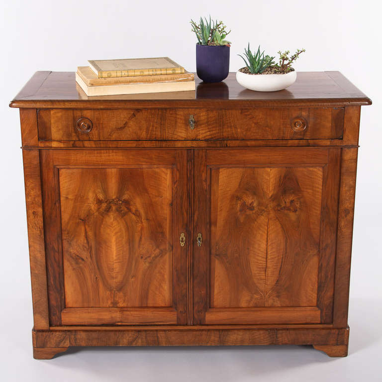 A gorgeous old cherry wood patina defines this classic 2-door Louis Philippe period Buffet. Found in Lyon, dating from the mid 1800's, the Buffet features paneled doors with exquisite burl book plated cherry wood and a single drawer with the
