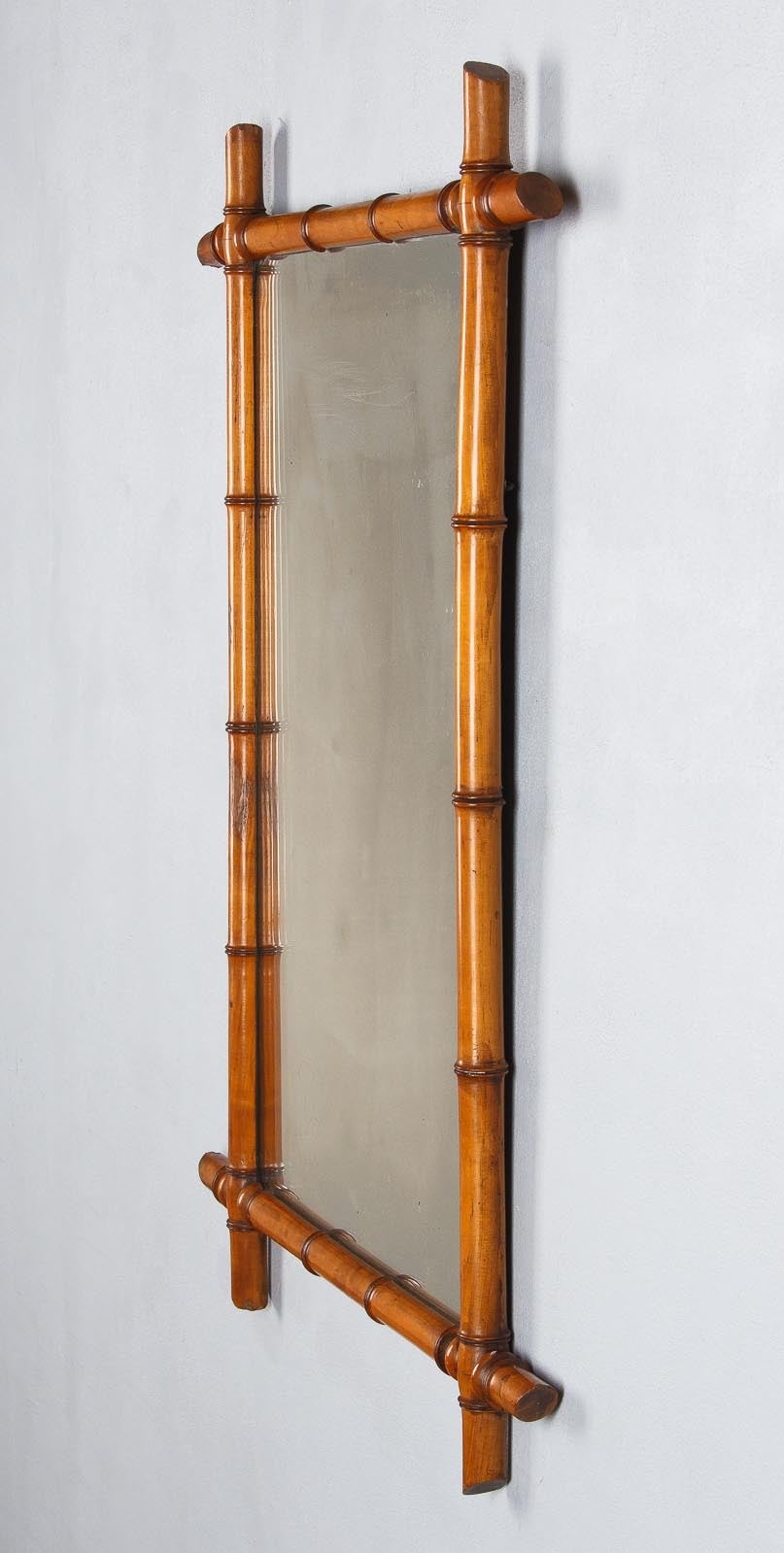 A French Colonial style mirror with a faux-bamboo frame made of cherrywood. The mirrored glass itself is 32" high x 20" wide.