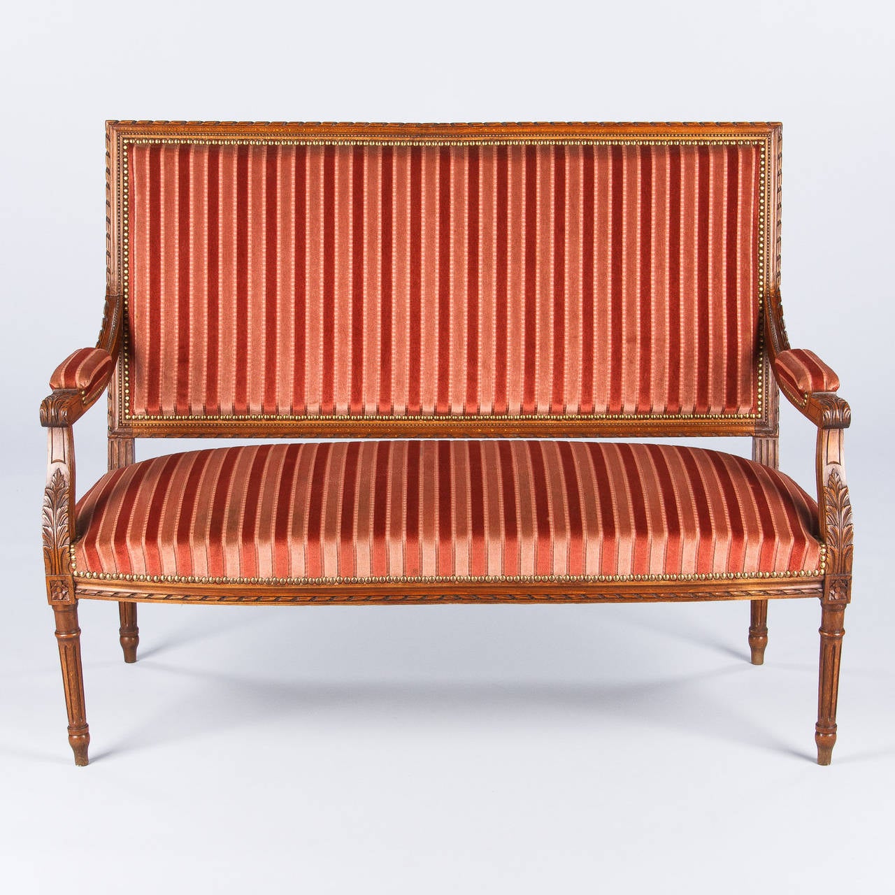 A Louis XVI style settee purchased from a private home in the Loire region. The settee is made of beechwood with fluted legs and delicate carvings including acanthus leaves, beading, fretwork and rosettes. The upholstery is striped fabric with