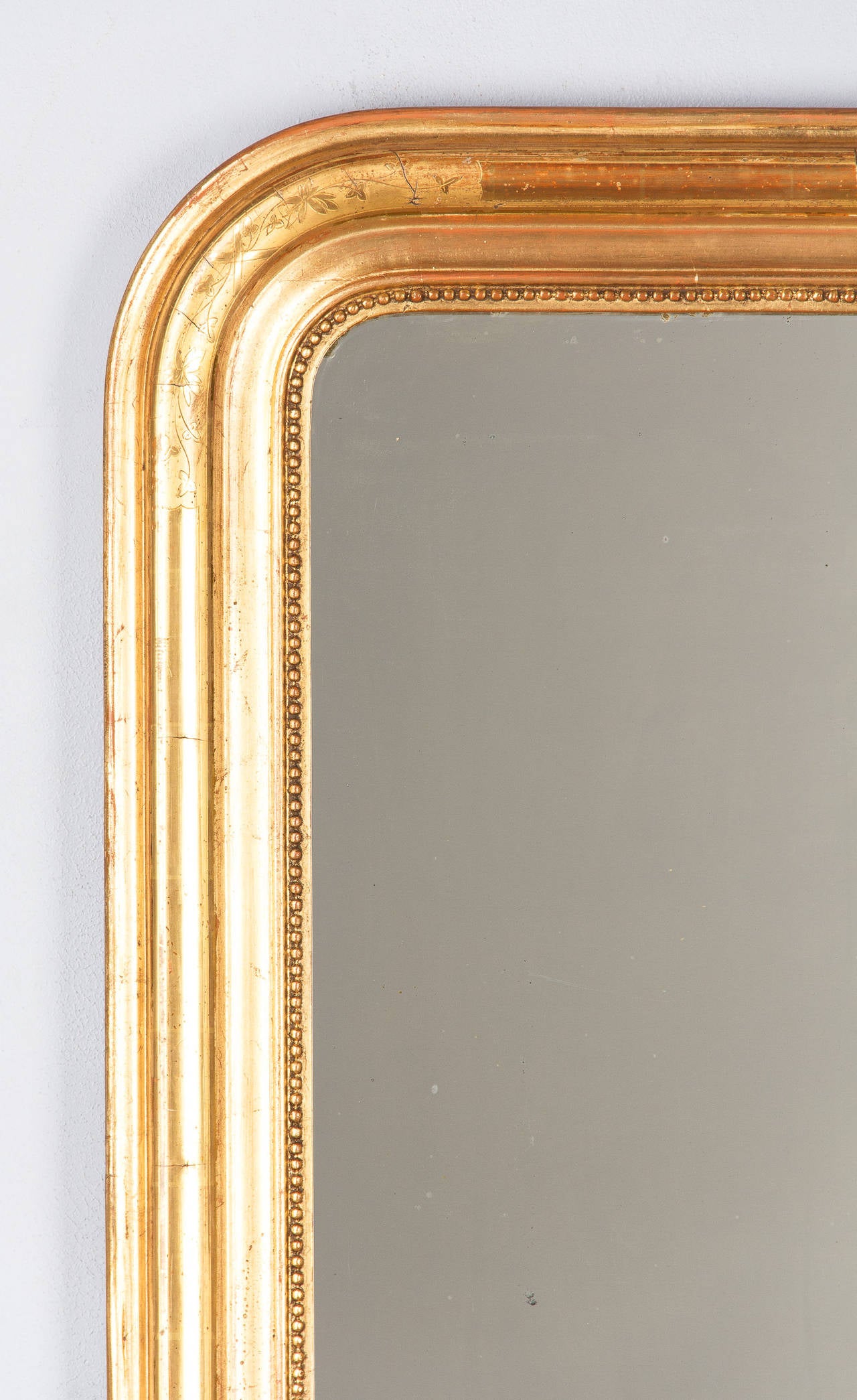 A lovely Gilded Mirror from the Louis Philippe Period, mid-1800s. The gold leaf wooden frame has a triple molding and is rounded at top, featuring subtle floral design at corners and a beaded trim around the glass. The mirrored glass is original.