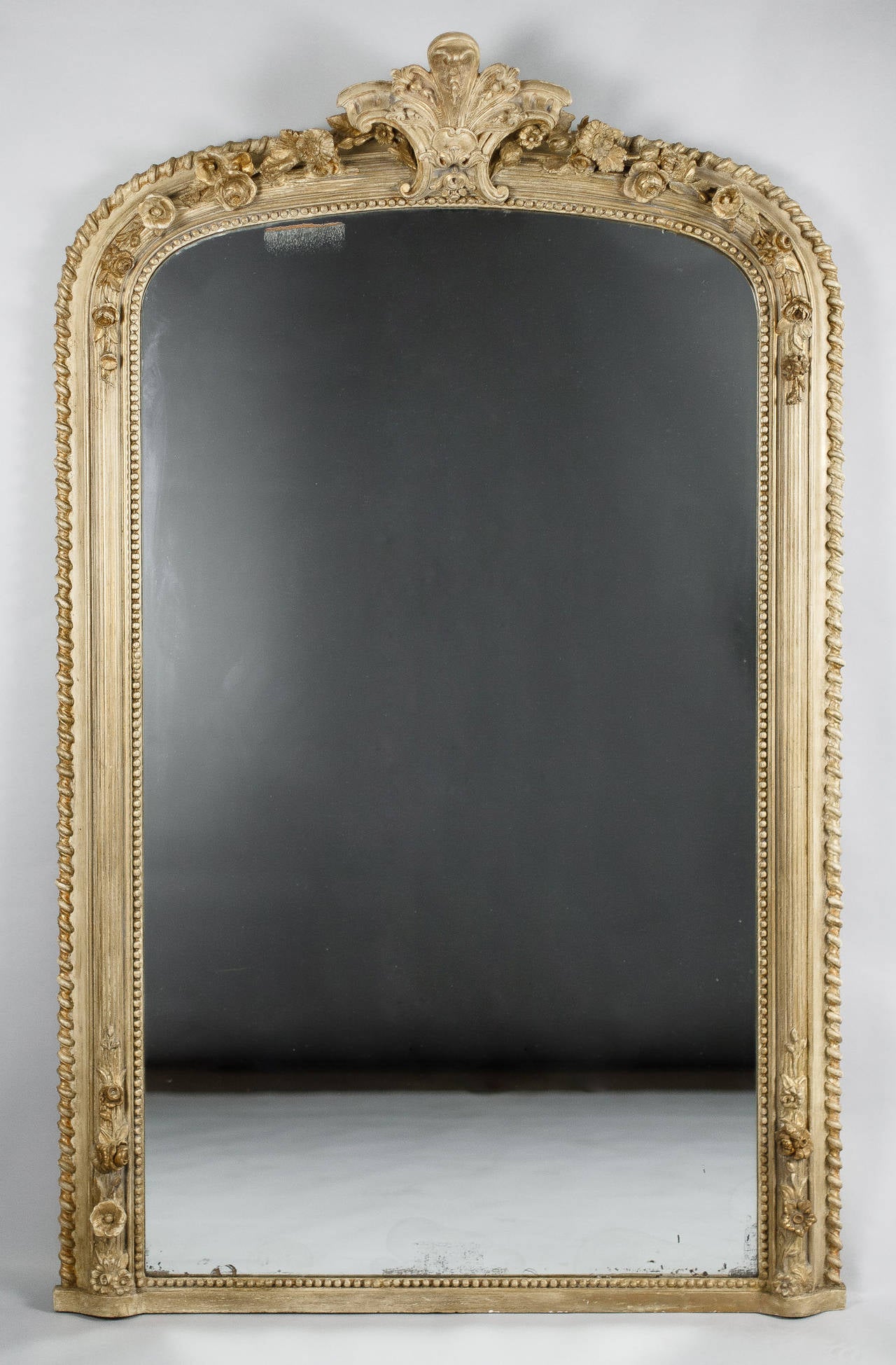 A great six foot tall mirror from the Napoleon III period that was painted off-white. The frame has an arched top with a cartouche in its centre and motifs of sculpted flowers. The frame also has motifs of beads around the mirror and scrolls at the