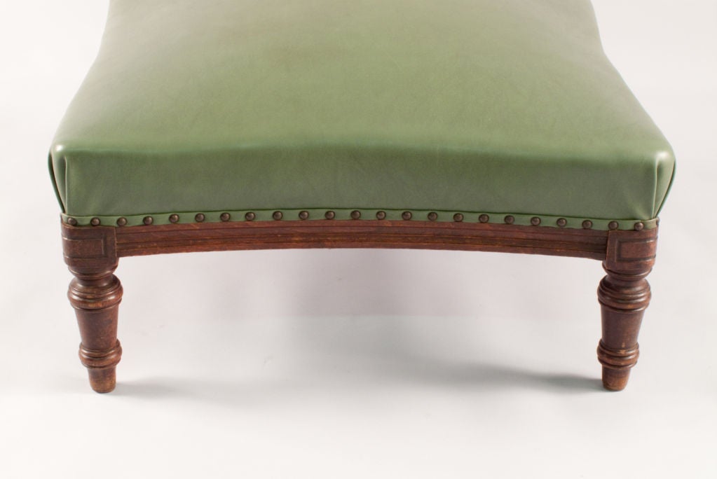 A square Ottoman from the early 1900's re-upholstered with an olive green vinyl top. The base and turned legs are walnut wood.