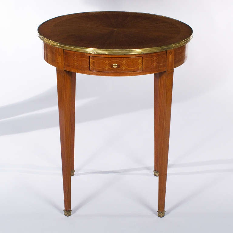 A wonderful Louis XVI Style round Table in mahogany and fruit woods veneer with exquisite marquetry. The top is brass-rimmed, the tapered legs are finished with brass sabots and the apron features a small drawer with a brass pull.