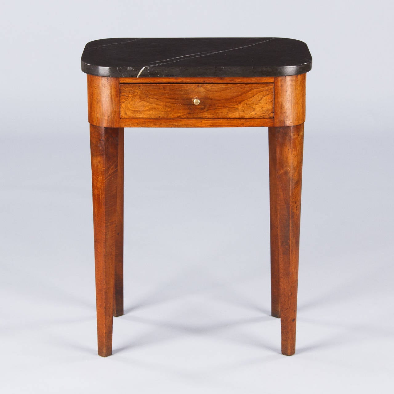 A petite Louis Philippe period side table purchased in Lyon. The walnut wood table features long tapered legs and the apron with rounded edges includes a drawer with a brass pull. The thick marble top is black with white veins.