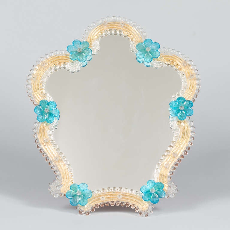 A Mid Century Venetian glass Vanity Mirror on a wooden easel stand. The shaped glass edge has a gold background and motifs  of blue flowers.