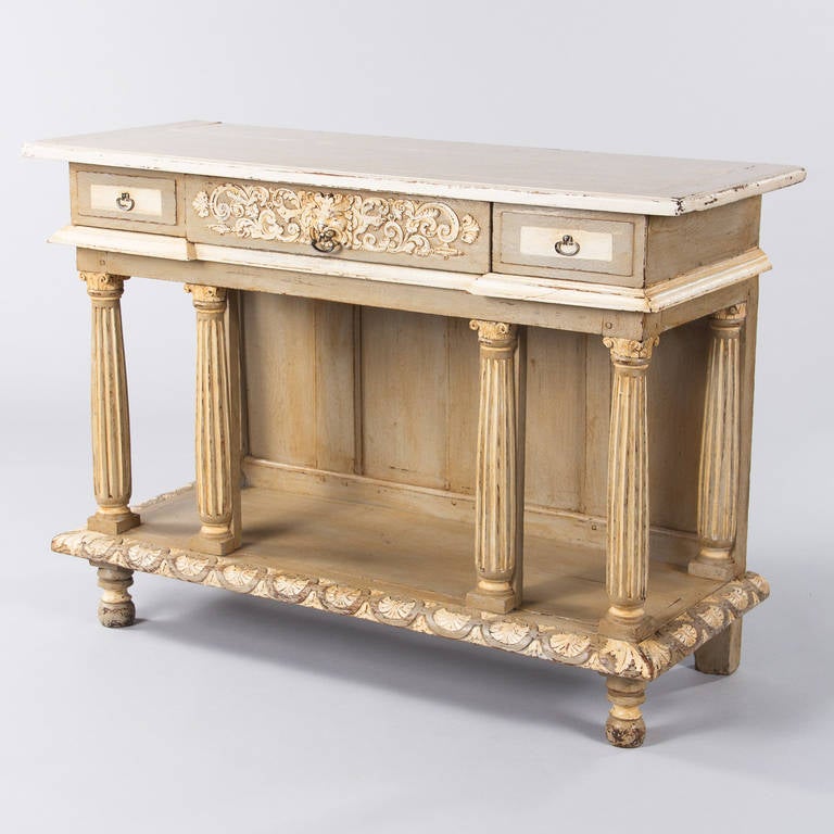 A late 1800s French Renaissance Revival sideboard or console table made of oak painted in off-white, cream and light grey tones. The console has three drawers in the apron with metal ring shaped pulls. The center drawer has carving of a lion head