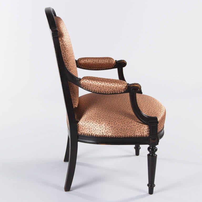 A Napoleon III period armchair in ebonized pearwood that was re-upholstered later with a patterned fabric in copper tones and antiques nails. The wide, comfortable armchair has an arched top, curvy fluted armrests with acanthus leaf carvings and