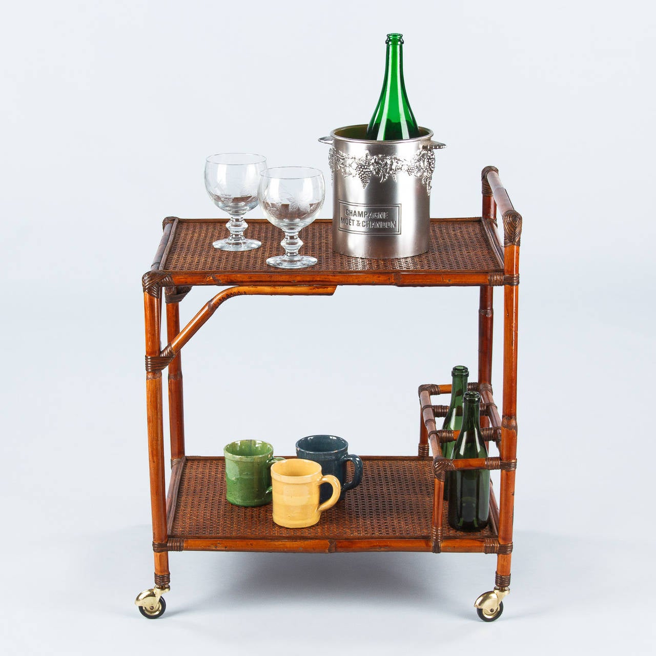 A nice bamboo bar cart with caned tops made in the French Colonial style, circa 1920s. The bottom shelf features a three-bottle holder and the cart rolls on brass casters with rubber wheels.