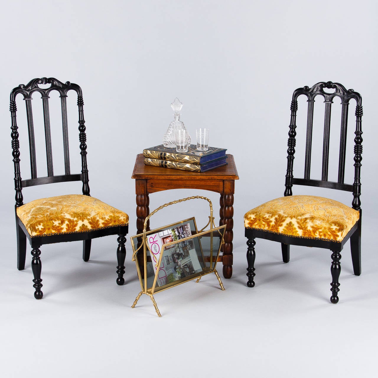 A pair of Napoleon III Chauffeuses, low chairs designed to sit by the fireplace, made of ebonized pear wood with their original floral upholstery. Dating from the 1870s, these chairs feature a slat back with a serpentine top rail and turned legs.