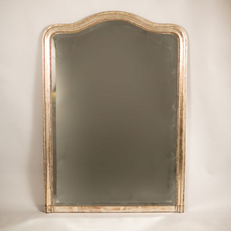 A 19th Century Louis Philippe Period Mirror with a silver gilt frame on wood and plaster. The top is arched and the mirror is beveled.