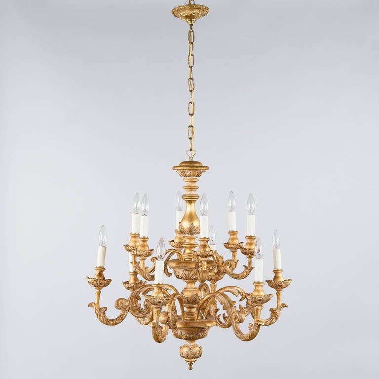 A twelve-arm chandelier in the Rococo style from Italy. The fixture is made of painted and gilded wood with scrolls, arabesques and acanthus leaves. There is a brass finial at the bottom center and an adjustable brass chain and canopy that add 22.50