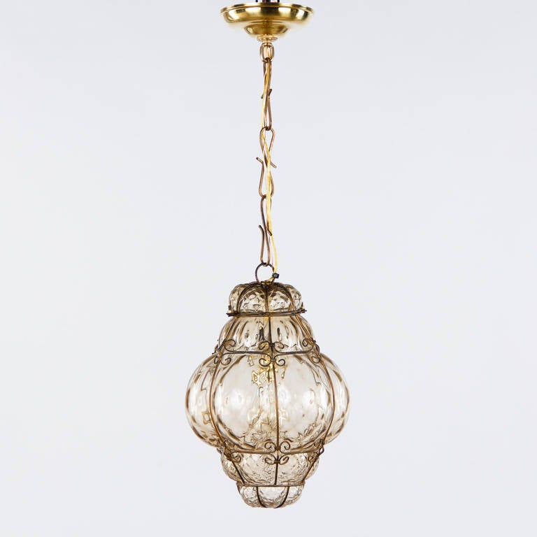 A 1940s Murano wire cage lantern with handblown bubble glass in light amber tones. The fixture is housing a single medium socket light bulb. The original chain and canopy add 14