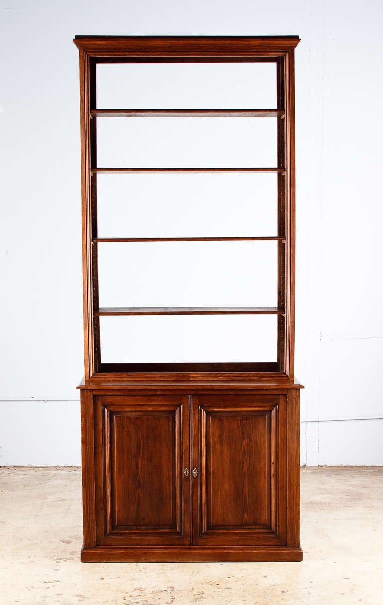 A simple but elegant and functional bookcase found in the Bresse Region of France. The bookcase is made of stained pine wood. The top part features 4 adjustable shelves and an open back. The bottom part is a 2 door cabinet with 1 single shelf