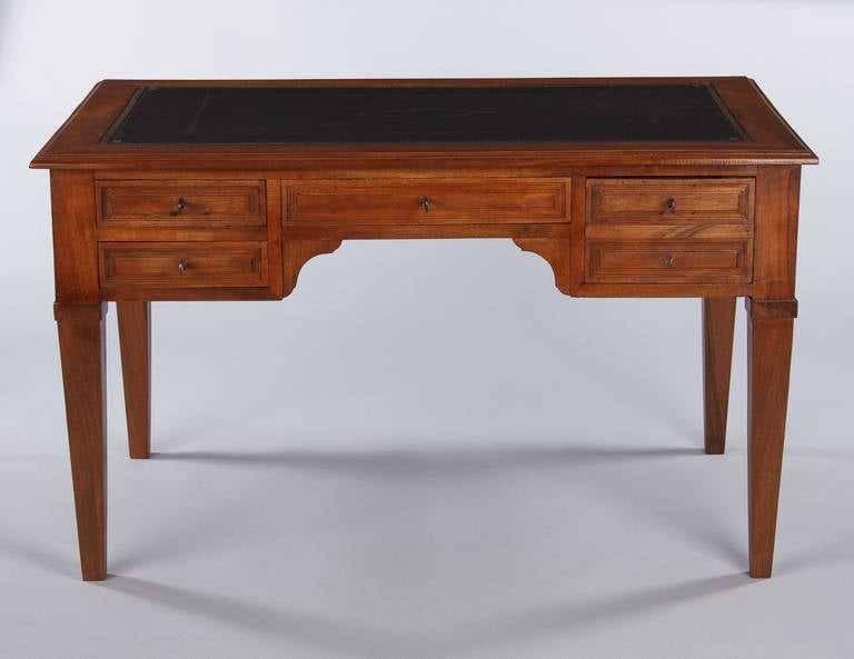 A gorgeous desk in the Directoire style made of walnut wood with an embossed black leather top. The desk has four drawers in the apron and two pull-out shelves on the sides (12