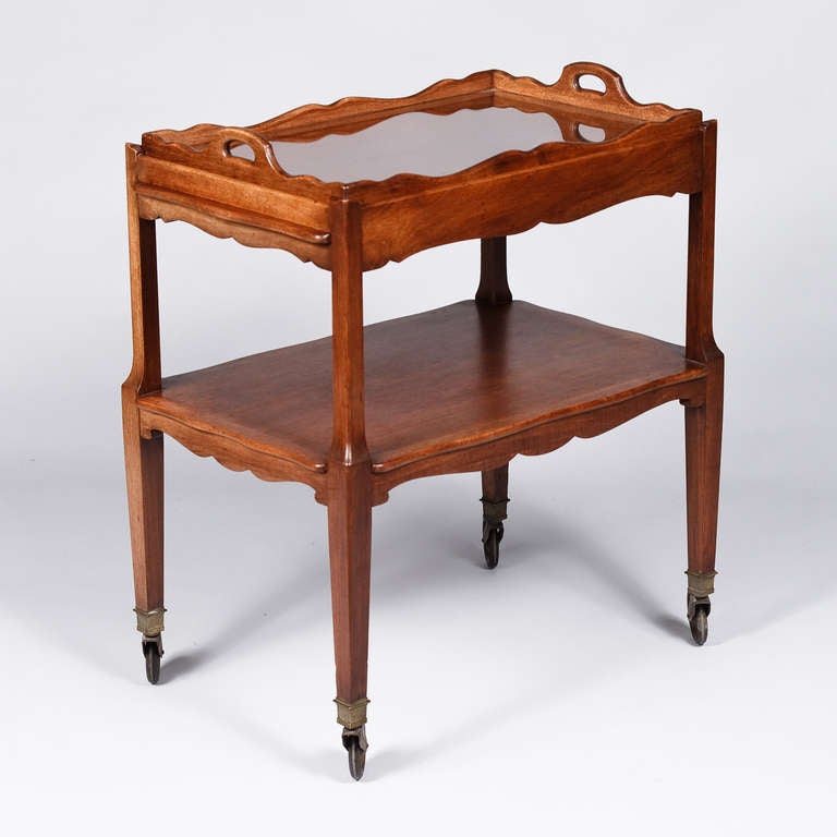 An early 1900's French Serving Table made of walnut with tapered legs and rolling on brass trimmed rubber wheels. The Bar Cart features include a middle shelf, two pull out shelves at both ends (9.5