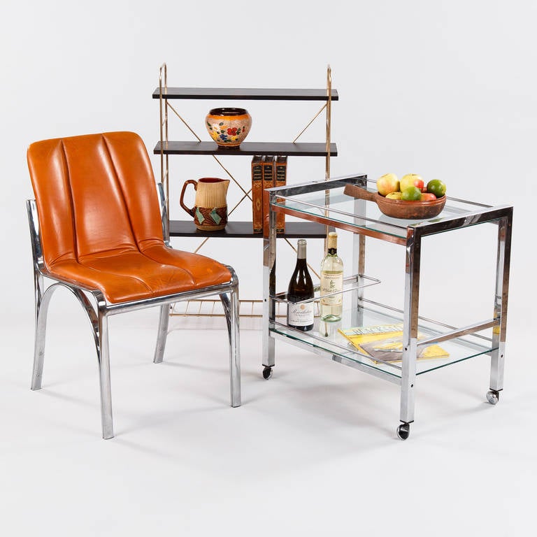 A vintage bar cart, circa 1970s, in polished chrome metal with two clear glass tops. The cart features a bottle holder and rolls on chrome and composite casters.