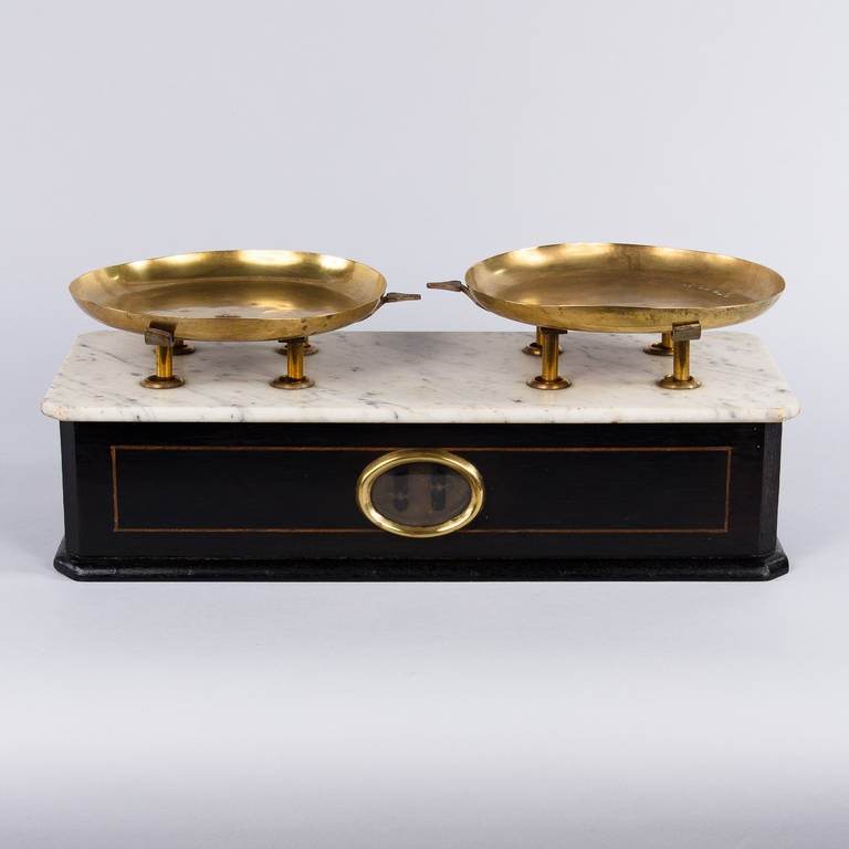 A bakery scale from the Napoleon III Period made of ebonized wood with brass inlay, a white marble top and two brass plateaux.