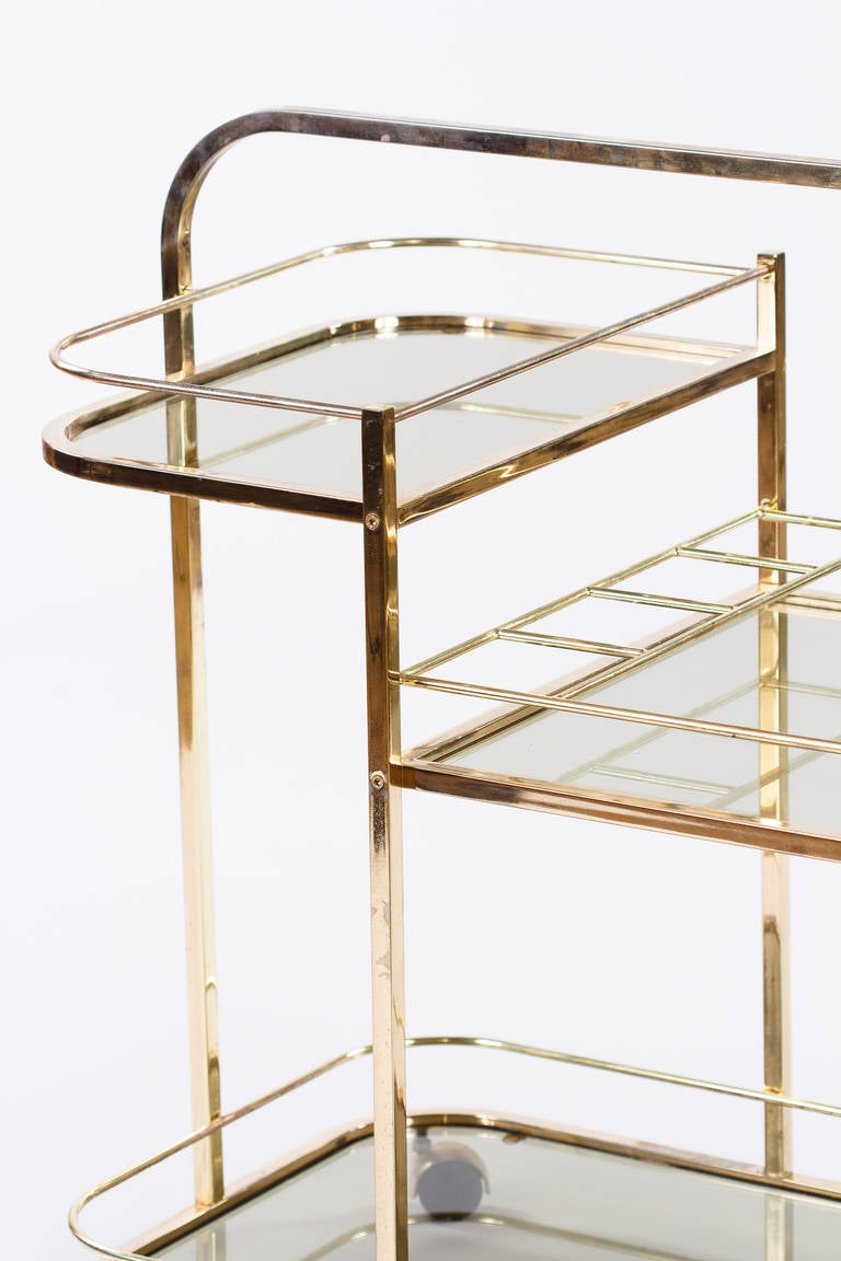 A vintage brass plated and lacquered bar cart with smoked glass tops. The cart features a 4 bottle holder and rolls on plastic casters.