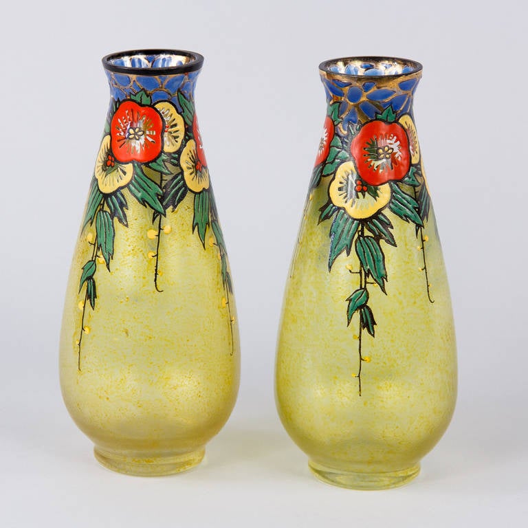 A colorful pair of Art Deco enameled glass vases signed by Becker and Richie, French circa 1930. Each vase has a short base and a wide, low belly that gently tapers as it goes up. The necks hit their narrowest just below a slightly flared rim. Much