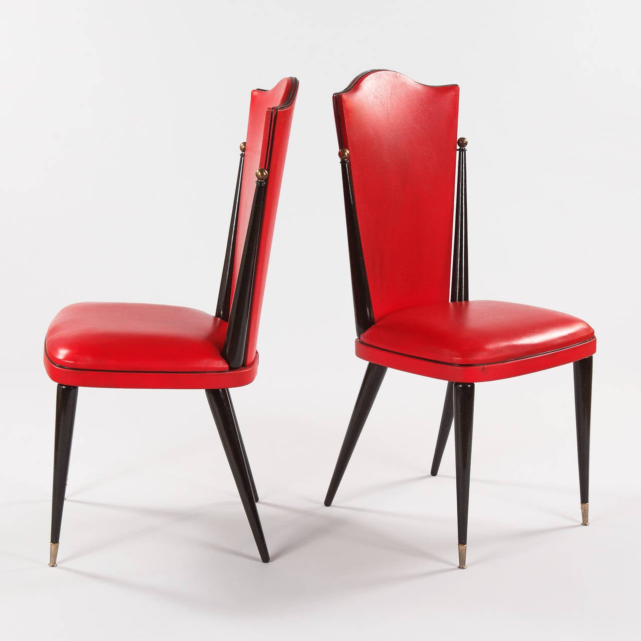 A pair of great looking vintage French chairs, circa 1960s, in red vinyl with a black lacquered wood frame. The chairs have a tall arched top back and the feet are finished with a brass sabot. From floor to seat: 18.50