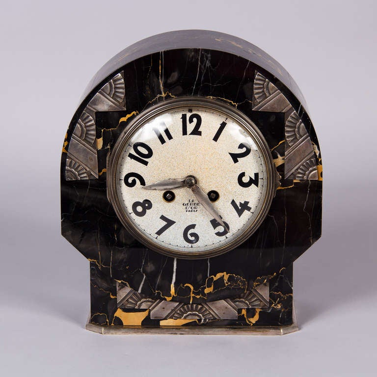 A beautiful French Art Deco Mantle Clock made by La Gerbe d' Or in Paris. The round shaped clock is made of black marble with gold veins and geometrical silver metal accents. Mechanism has an 8 day movement.