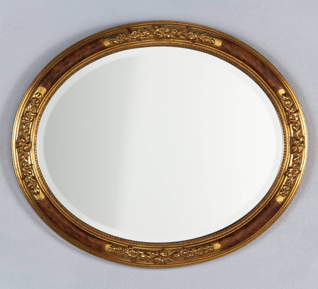A delightful Oval Mirror in the Louis XVI style, circa 1930's, that can be hung vertically or horizontally. The mahogany frame has gilded accents with flower motifs. The beveled glass has a beaded edge.